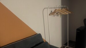 Una habitación con un sofá verde oscuro, un perchero metálico blanco con perchas de madera y un altavoz negro.