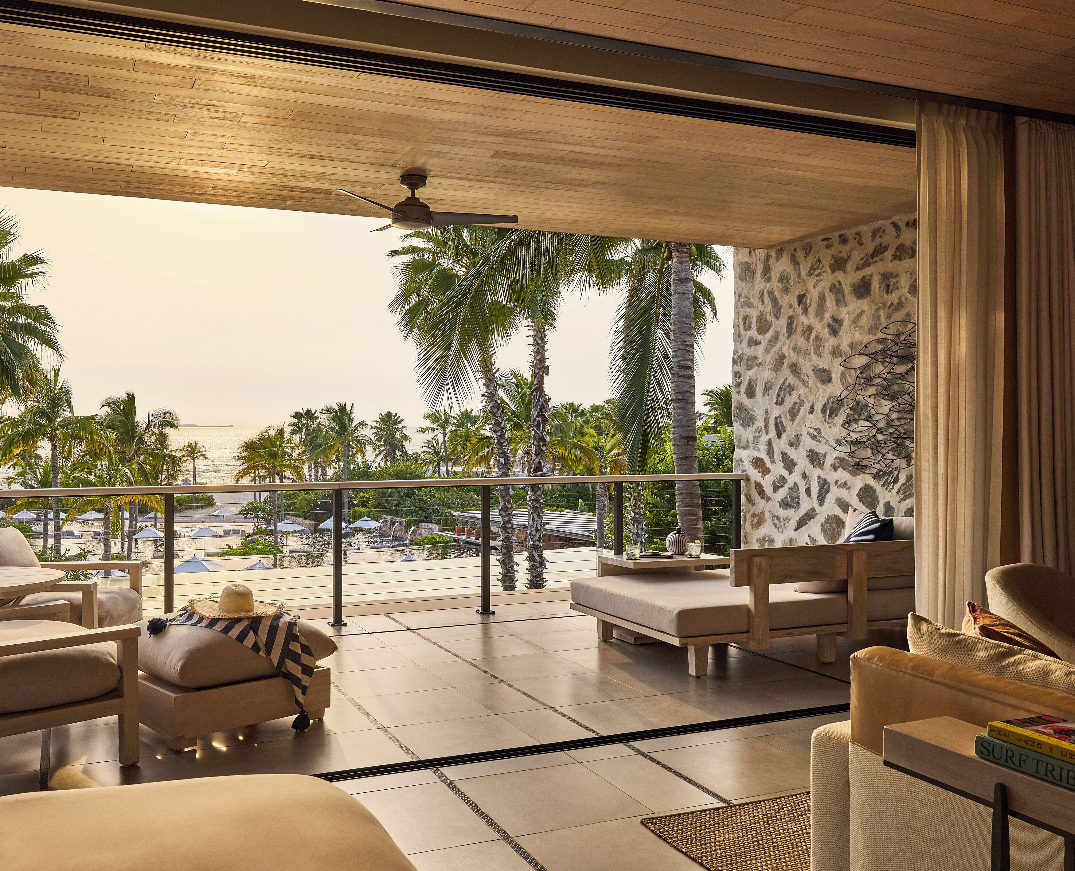 Habitación de hotel moderna con balcón que da a una piscina, palmeras y vistas al mar.