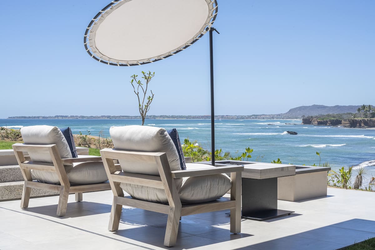 Un patio frente al mar con dos sillas de madera y una mesa, con vistas al océano.