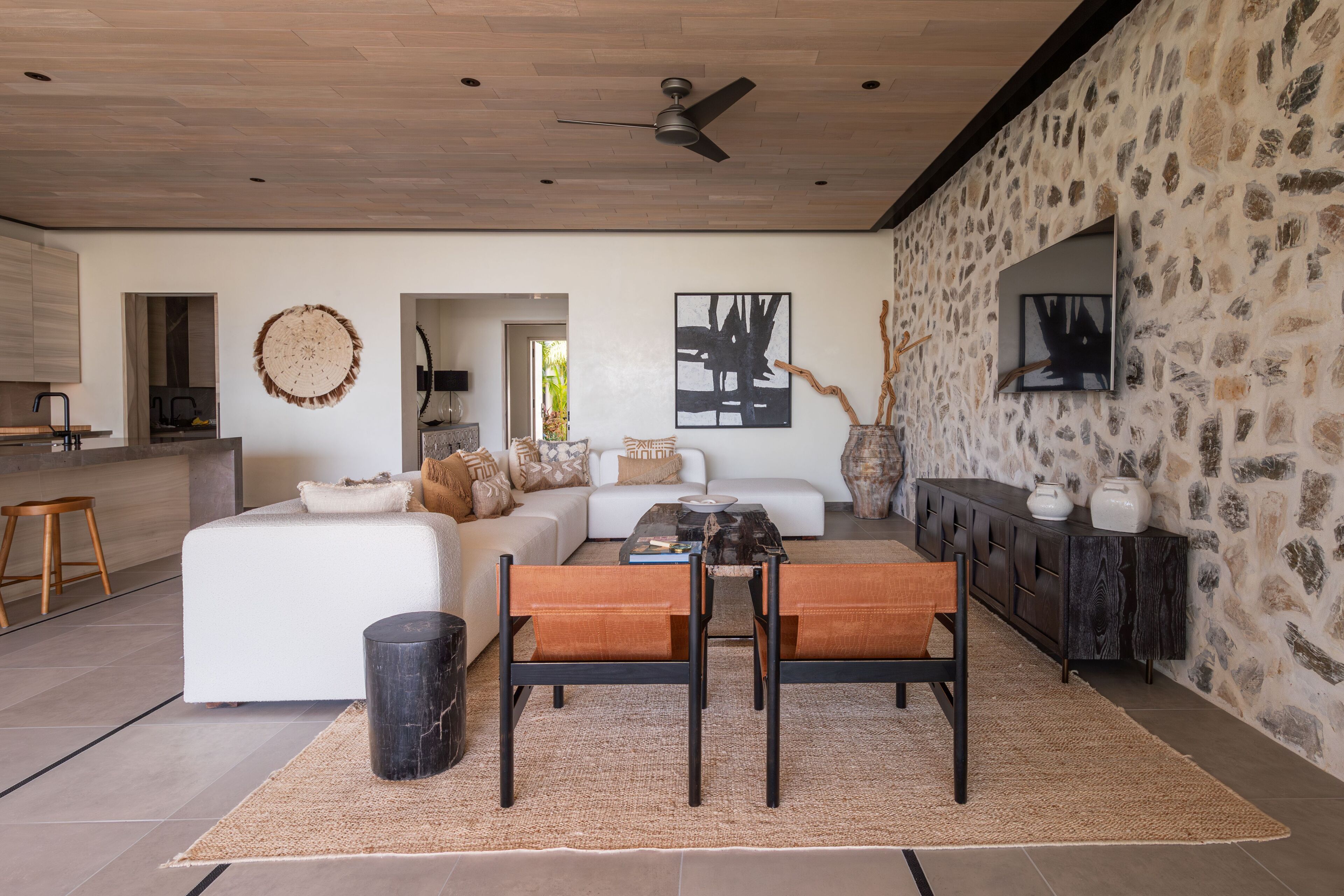 A modern living room with a white sofa, a dining table with chairs, a black trash bin, and a stone wall with artwork.