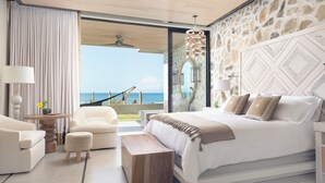 Un dormitorio con una cama grande, vista al océano y una pared de piedra.