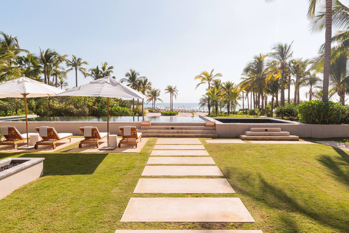 Zona de piscina con sillones y sombrillas, vista despejada al océano y palmeras.