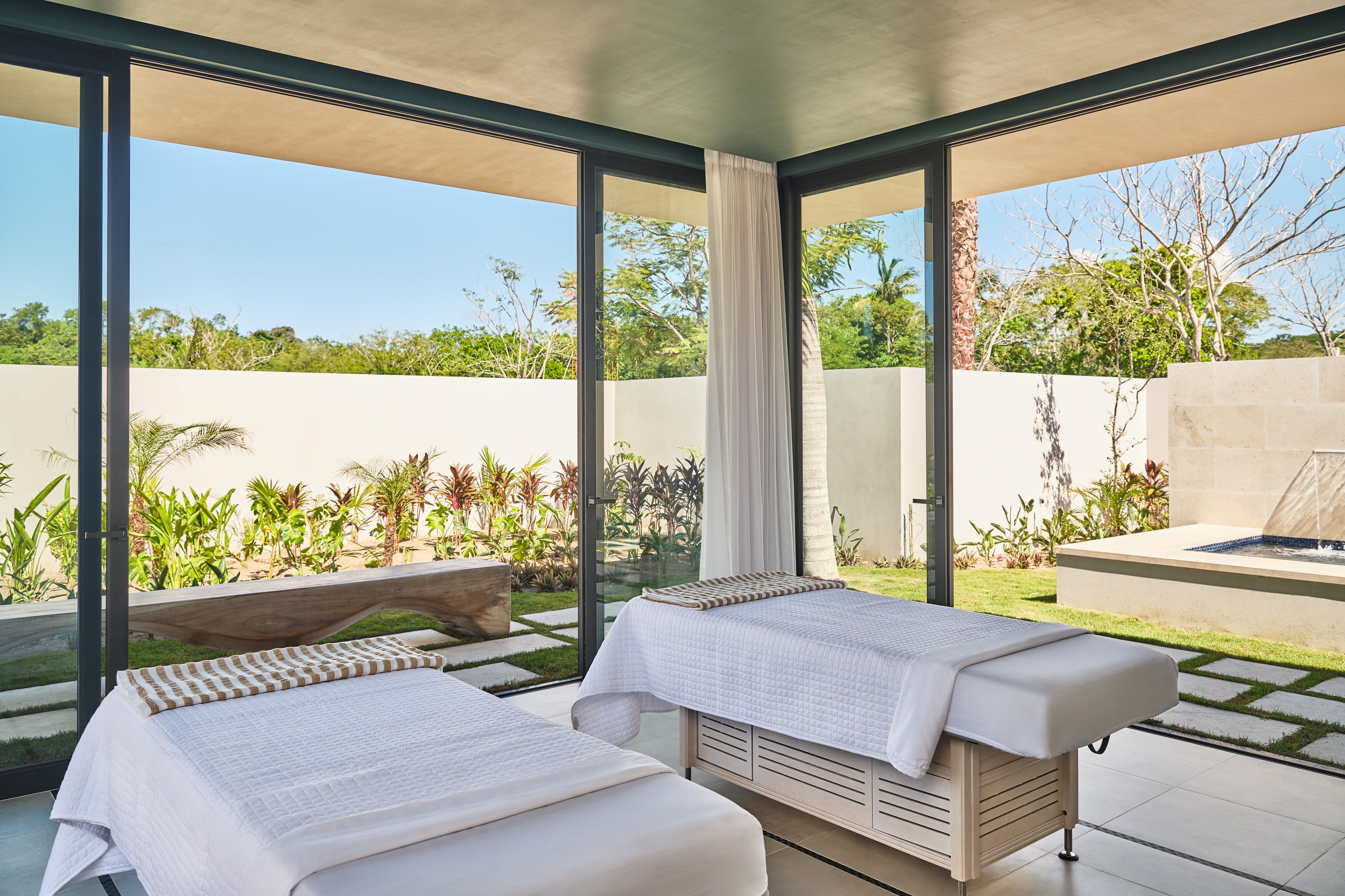 A room with two massage tables, large windows, and a view of a garden.