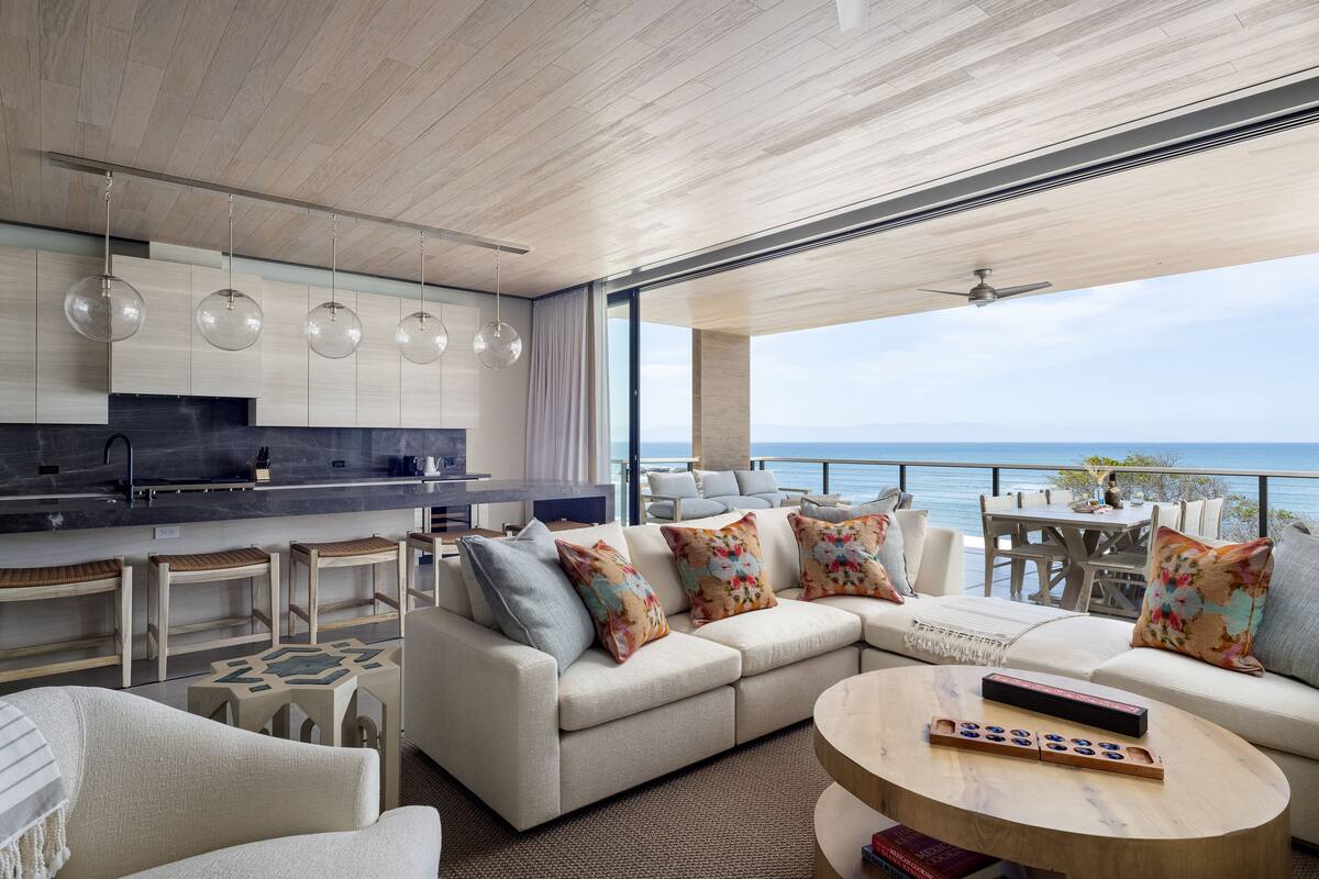 Un salón moderno con sofá, mesa de centro y mesa de comedor, con vistas a un paisaje marino.
