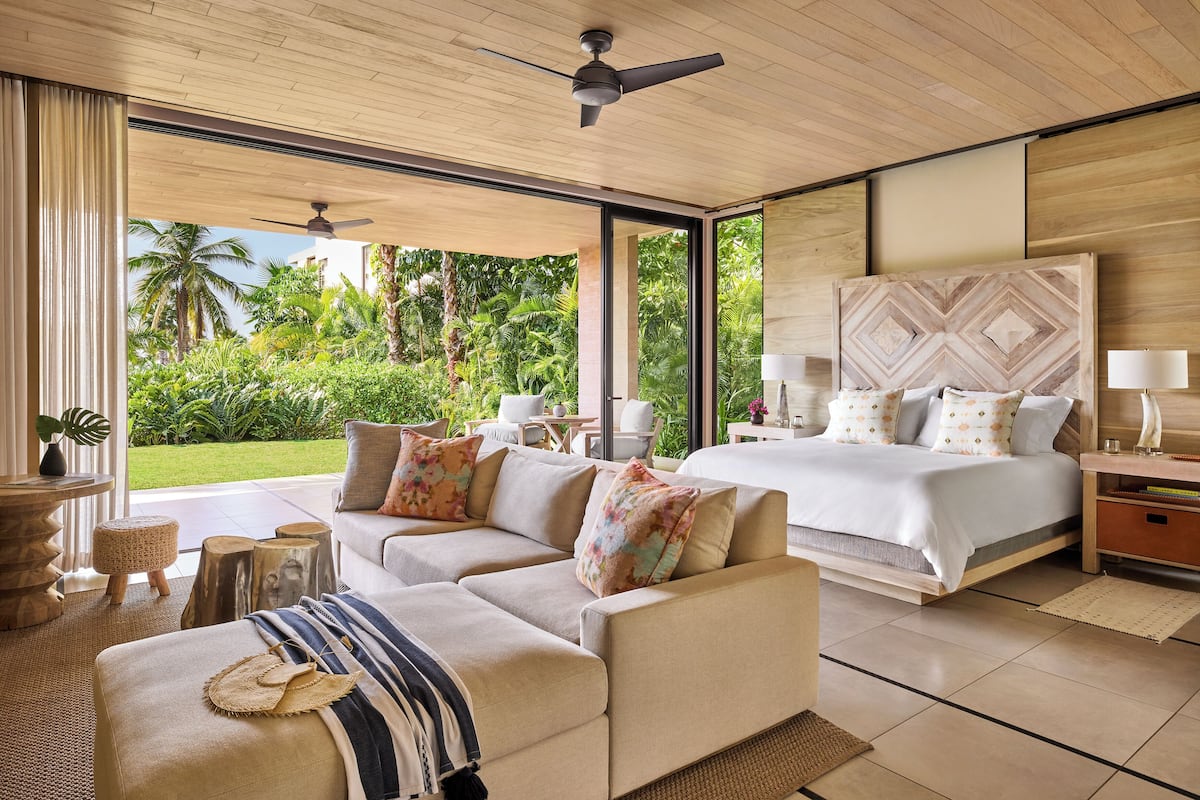 Un dormitorio moderno con una cama grande, un sofá y vistas a un jardín tropical.