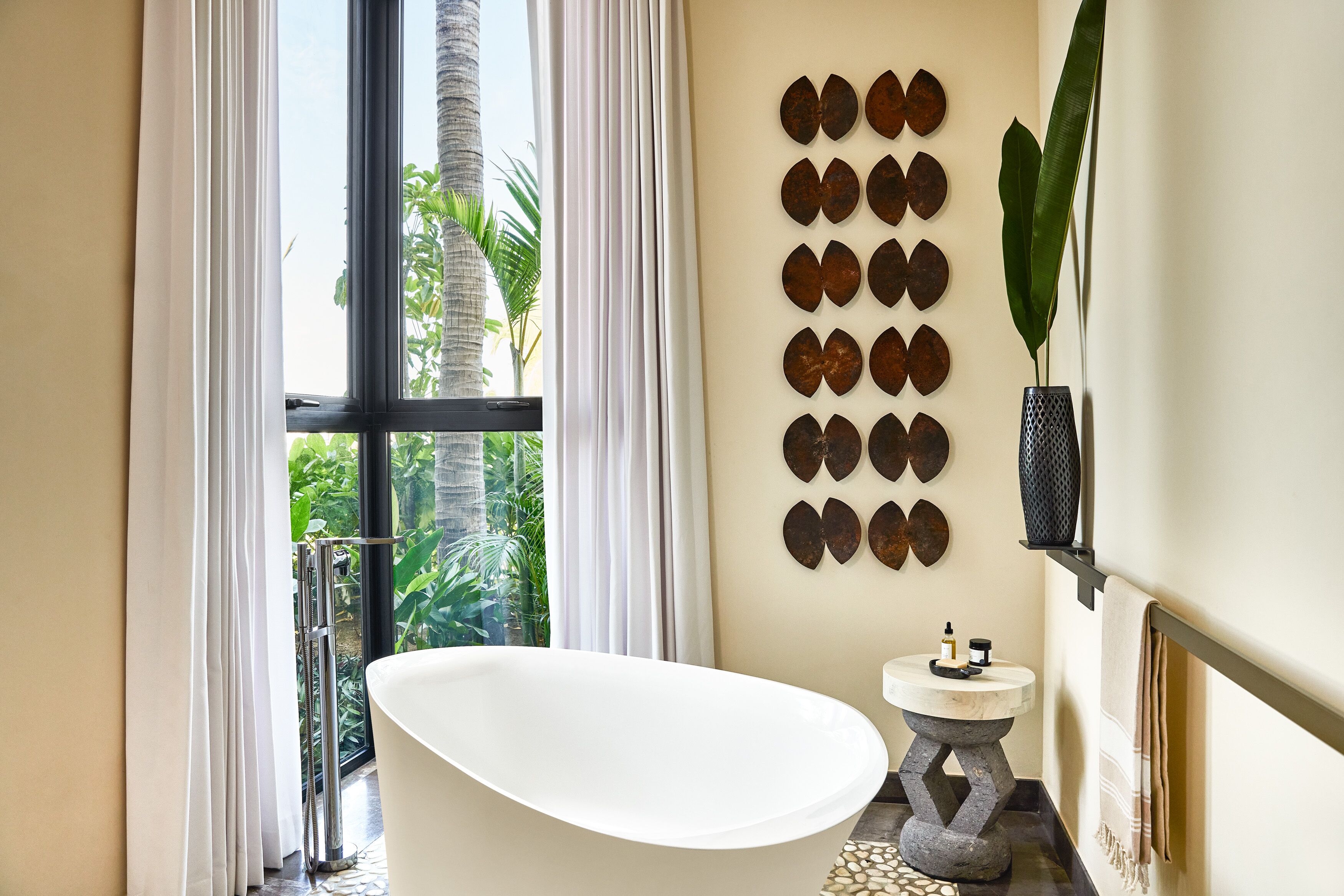 Een moderne badkamer met een vrijstaand bad, een klein rond wastafeltje en een decoratieve wand met ronde spiegels.
