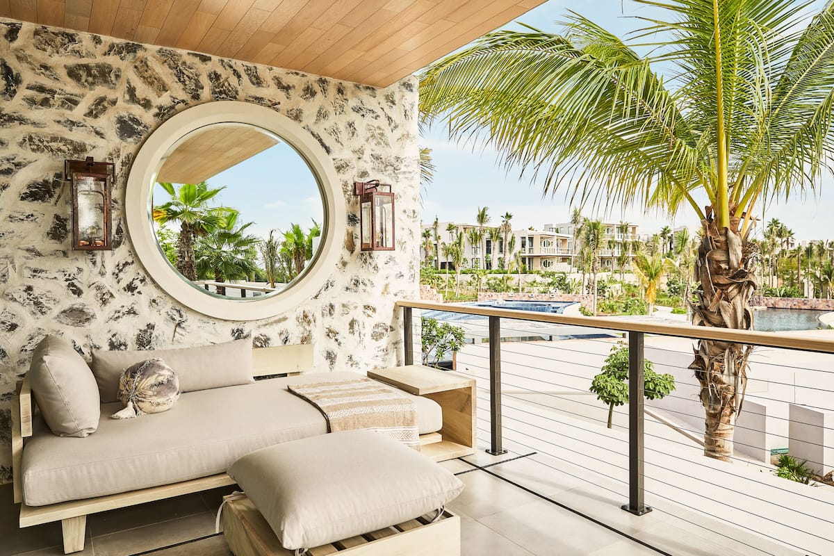 Un balcón con un sofá, un espejo redondo y vistas a una piscina y palmeras.