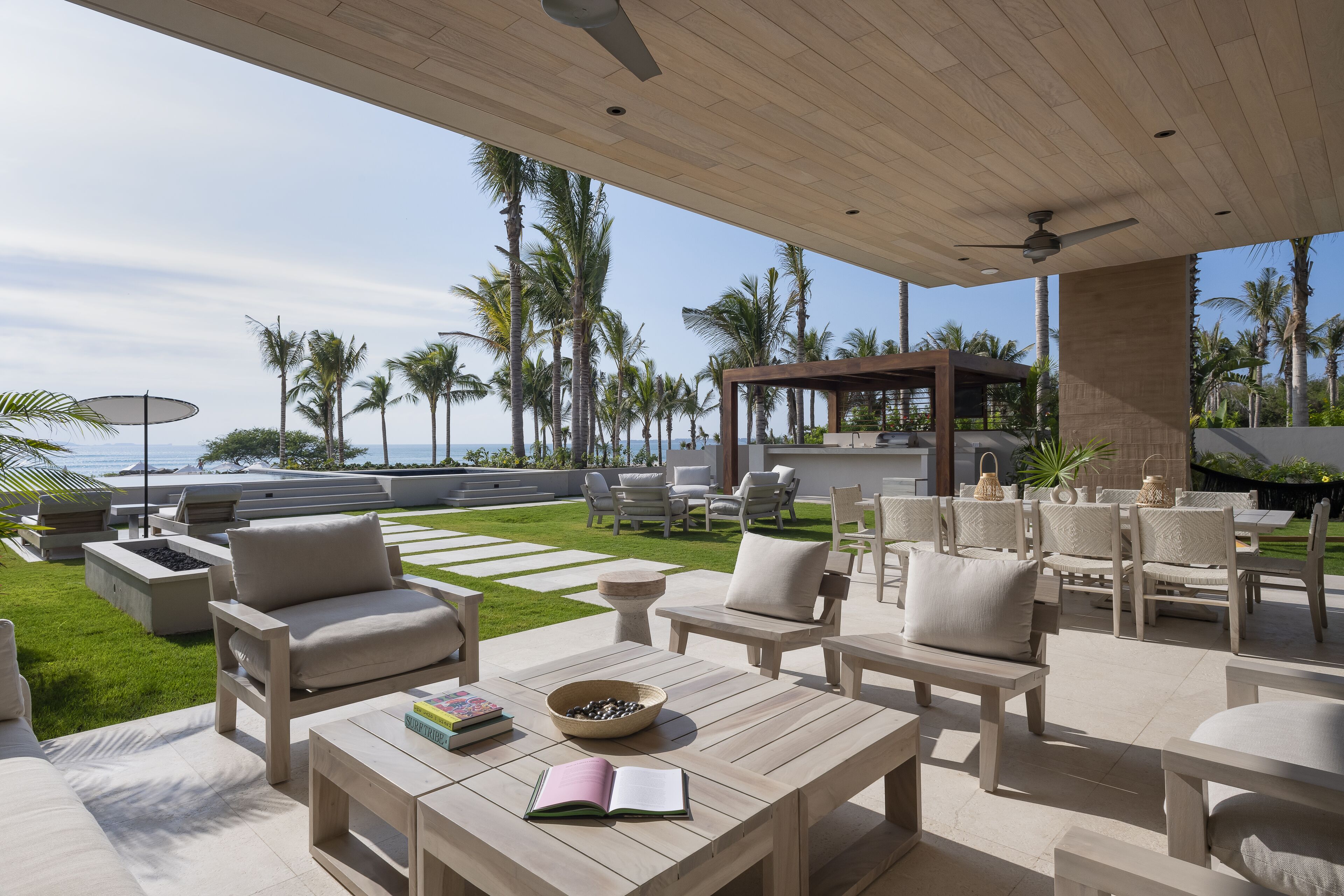 Un patio exterior con muebles de madera, una pérgola y vista al océano.