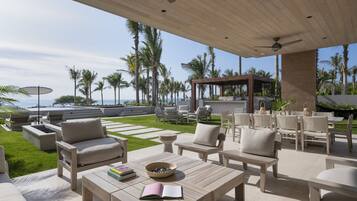 Un patio exterior con muebles de madera, una pérgola y vista al océano.