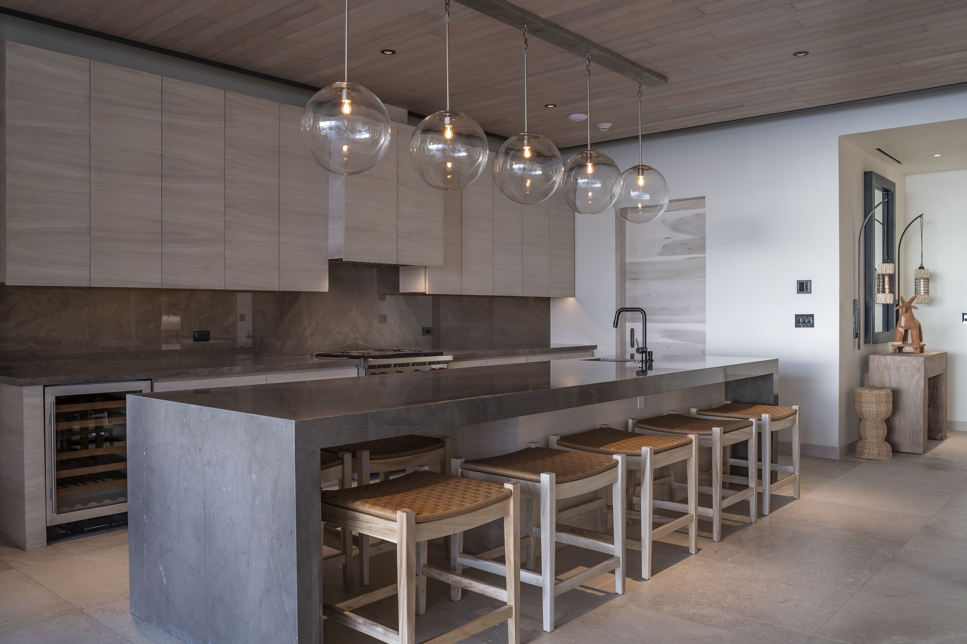 Una cocina moderna con una isla grande, taburetes de bar e iluminación colgante.