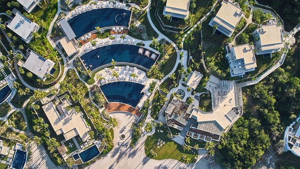 Vista aérea de un complejo turístico con varias edificaciones, una zona de piscina central y acceso directo a la playa.