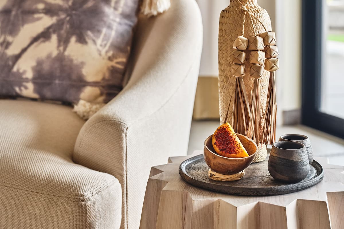 Una sala de estar acogedora con un sofá color beige, un jarrón decorativo tejido y una bandeja con un cuenco de fruta y dos tazas pequeñas.