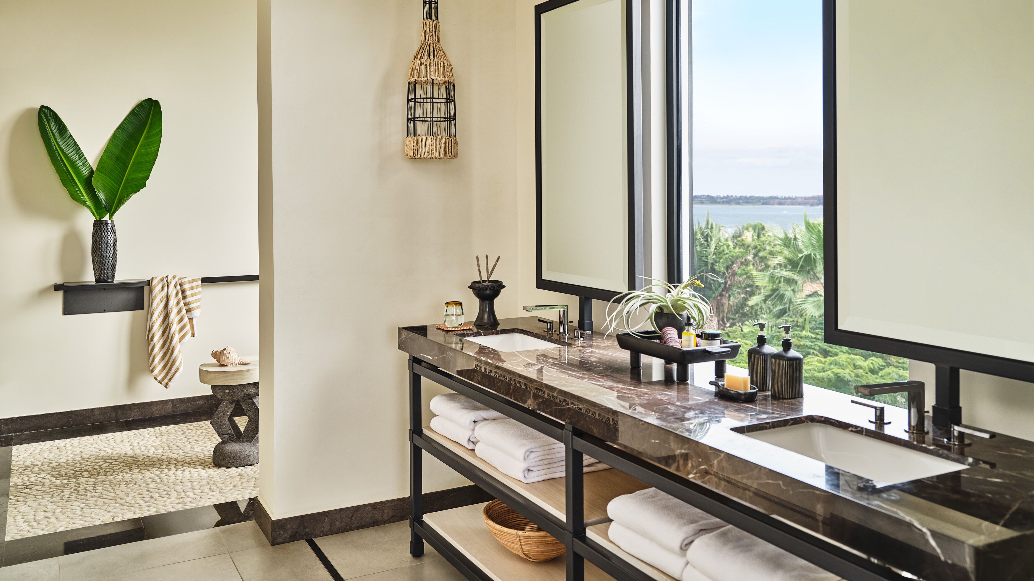 A modern bathroom with a large mirror, two sinks, a marble countertop, and a view of the outdoors.