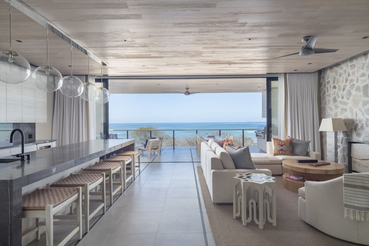 Un espacio de sala moderno con cocina, asientos tipo bar y vista al océano.