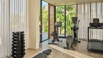 A modern gym with exercise equipment, large windows, and a view of greenery.