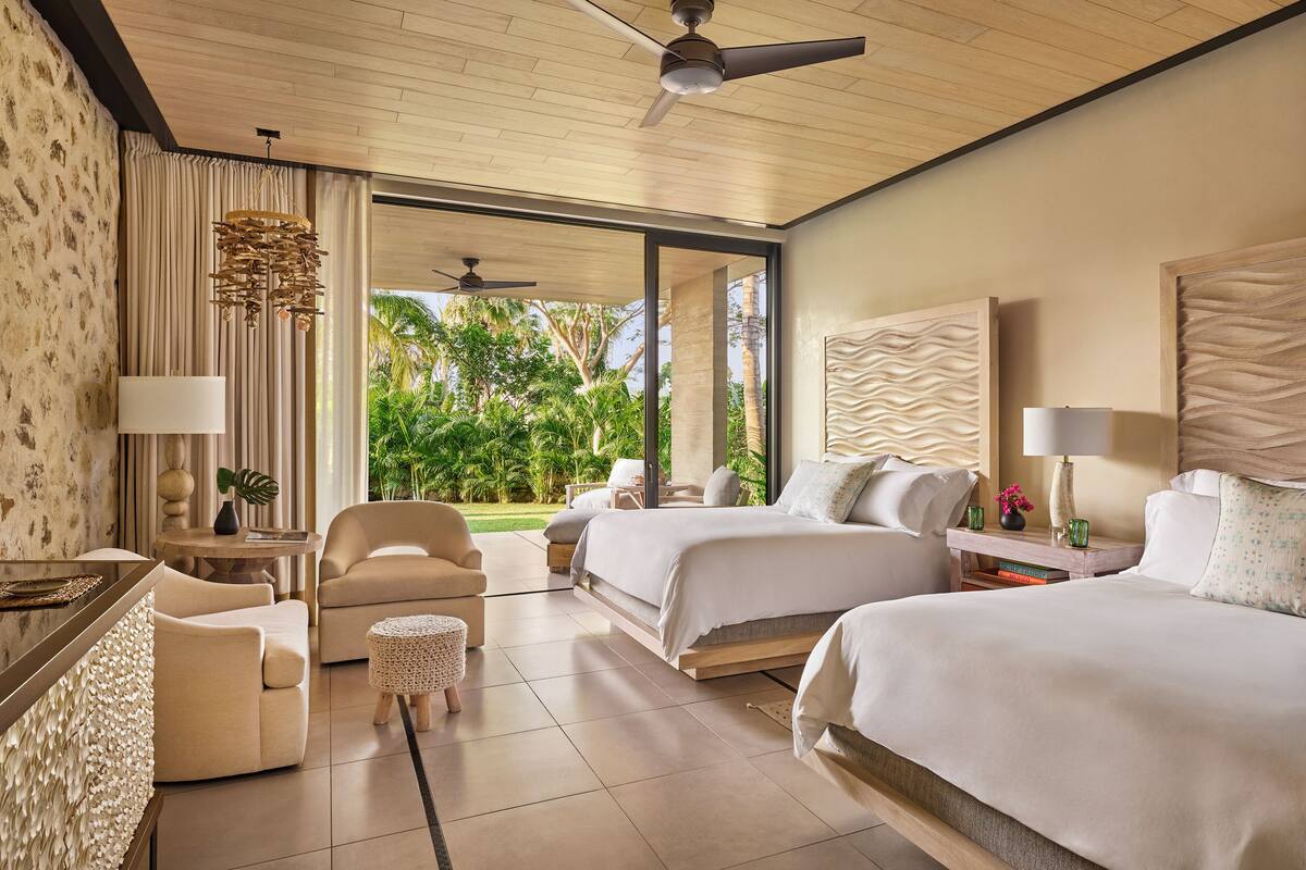 Una habitación de hotel con cama, sofá, sillón, una mesita y un ventilador de techo.