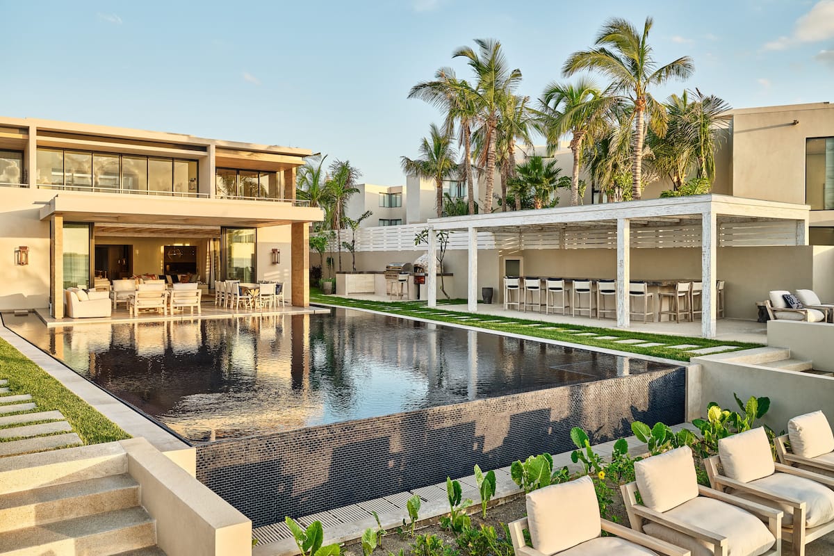 Un área de piscina moderna con una piscina cristalina, mobiliario exterior y palmeras.