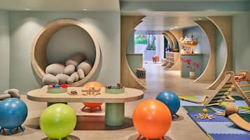 Zona de juegos infantiles con pelotas de ejercicios, una estructura de madera y una amplia zona circular de asientos.
