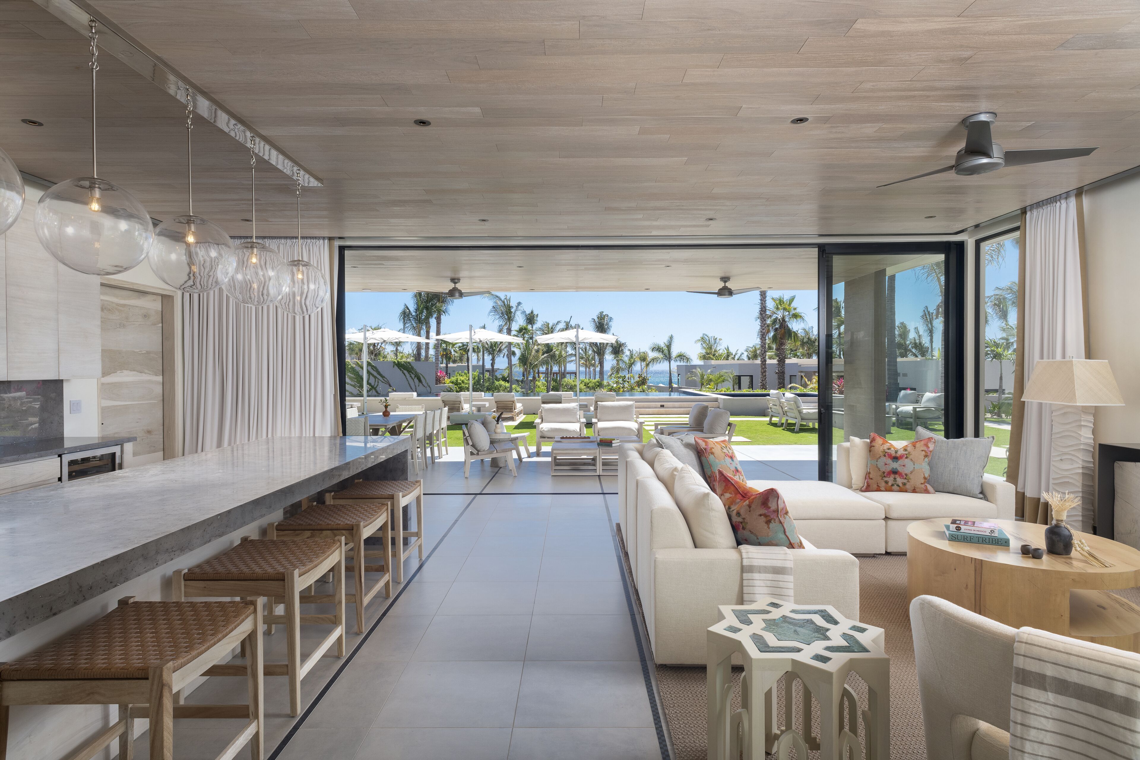 A modern living area with a kitchen bar, seating arrangements, and a view of the outdoors.