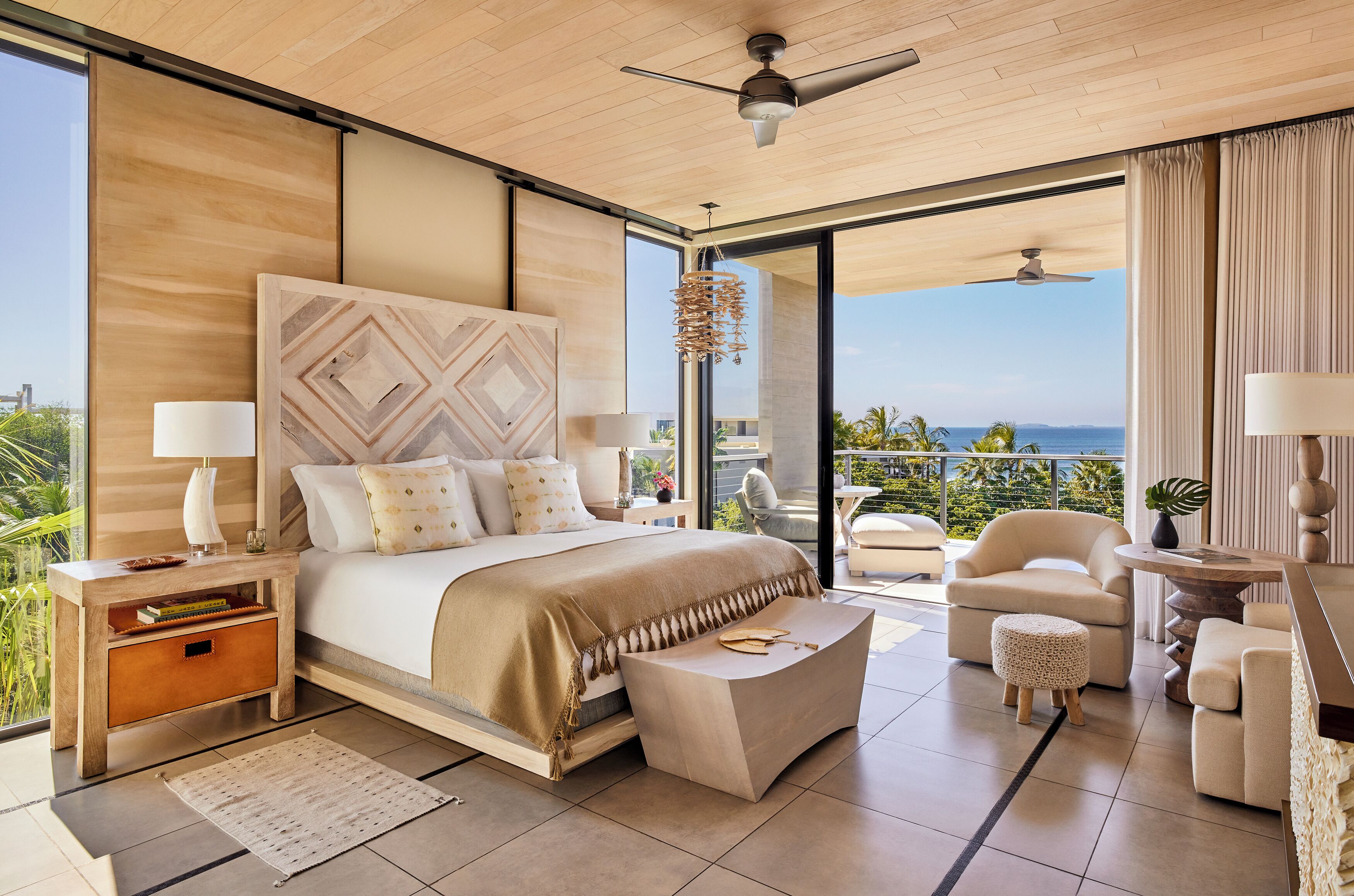 Un dormitorio moderno con una cama grande, una mesita de noche, una silla, un pequeño reposapiés y vistas al exterior.