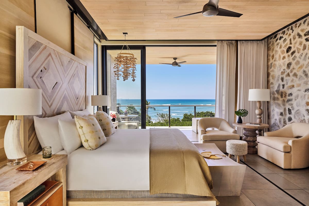 Habitación de hotel moderna con una cama grande, zona de estar y balcón con vistas al océano.