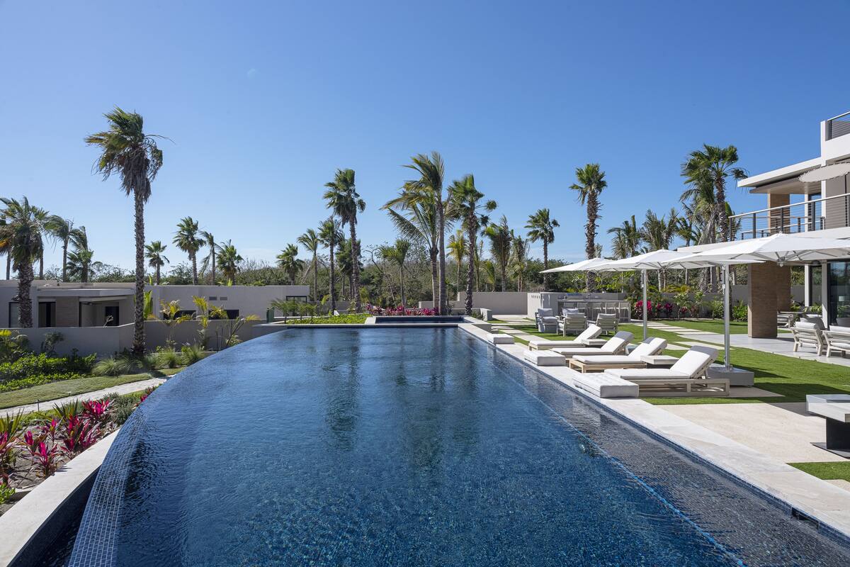 Una piscina con sillones de descanso y palmeras.