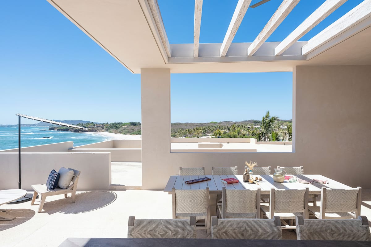 Una terraza con mesa y sillas, vista al océano y cielo despejado.