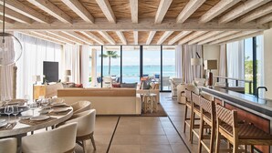 Amplia sala de estar con un sofá grande, mesa de comedor y sillas, con vistas a un paisaje marino.