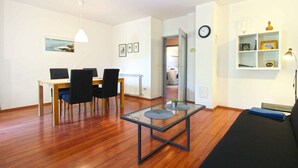 A modern living room with a dining area, a glass-top coffee table, a black sofa, and a bookshelf. - Holiday home mit Terrasse und Grill (Pula)