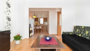 A living room with a sofa, a table with a decorative item, a potted plant, and a view into the kitchen area. - Holiday home with terrace and barbecue (Premantura)