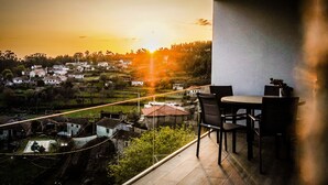 A balcony with a view of a village at sunset, a table with chairs, and a potted plant.