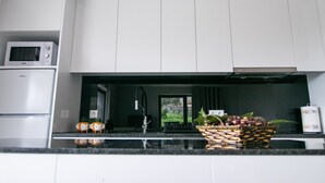 A modern kitchen with white cabinets, a black countertop, a microwave, a sink, and a basket of fruit.