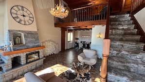 A rustic interior with a stone fireplace, a wooden staircase, a high ceiling, and a cozy seating area. - EVASION Gîtes & Spa – A unique getaway in the heart of the Vosges (Saint-Léonard)