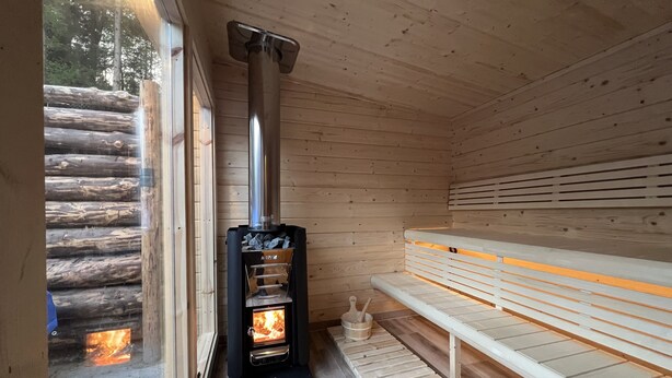 A wooden cabin with a wood-burning stove, a bench, and a window. - EVASION Gîtes & Spa – A unique getaway in the heart of the Vosges (Saint-Léonard)