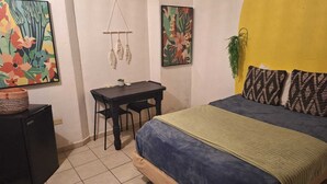 A bedroom with a bed, a desk, and two paintings on the wall.