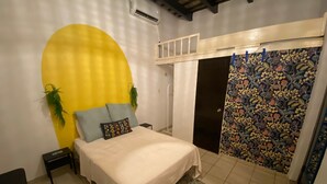 A bedroom with a bed, a nightstand, a potted plant, a wall-mounted air conditioner, and a door with a floral-patterned curtain.