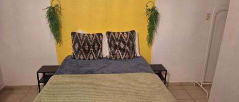 A bed with a green blanket, two patterned pillows, and a yellow wall.