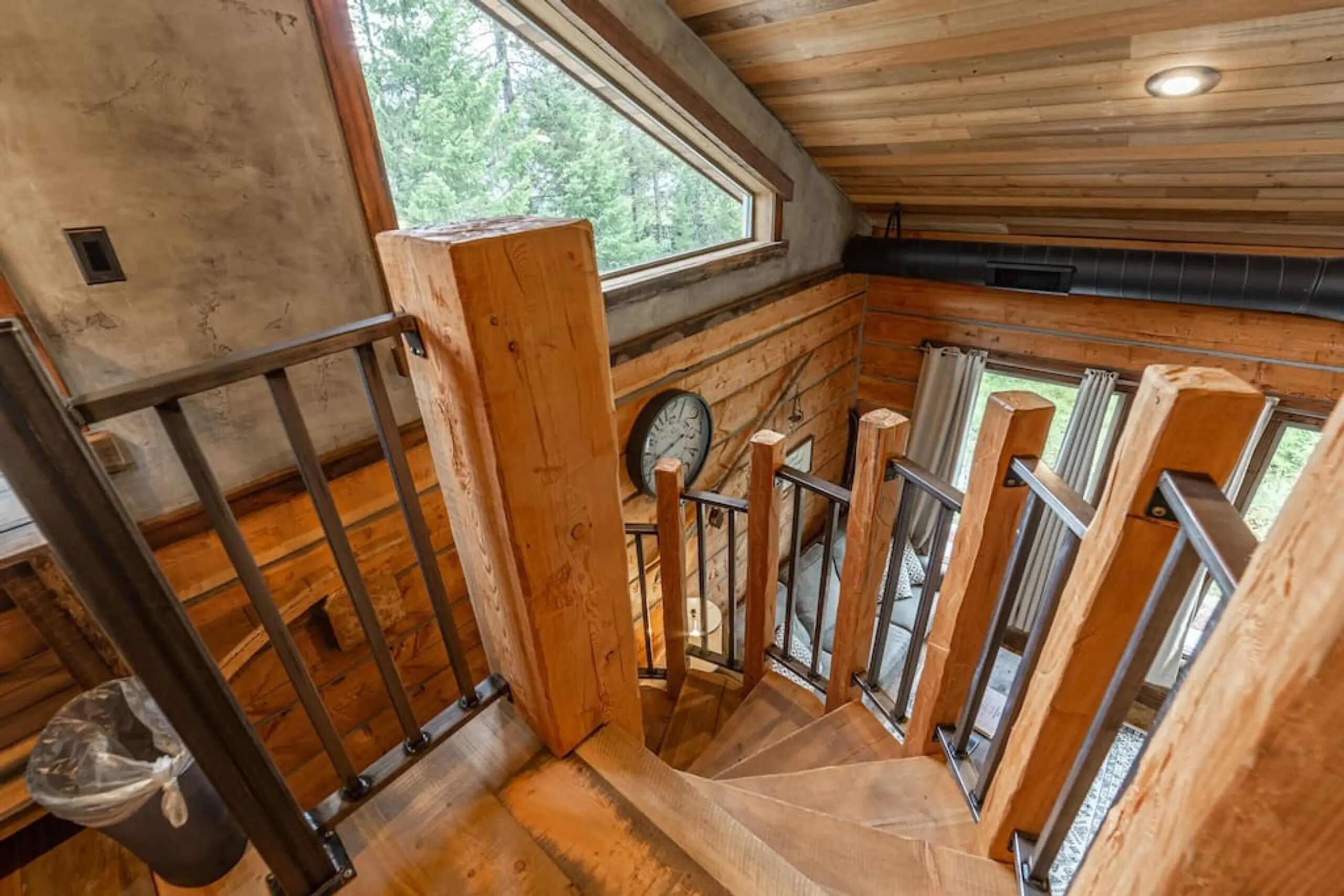 A wooden interior with a spiral staircase, a clock, and a window.
