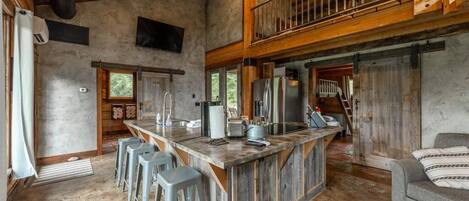 Una cocina rústica con una isla central, taburetes de bar y techo de madera.