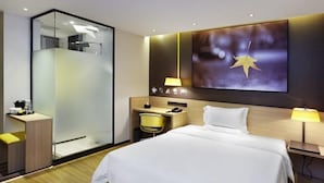 A modern hotel room with a bed, bedside tables, a desk, a chair, a glass shower enclosure, and a large wall-mounted artwork. - IU Hotel (Shanghai)