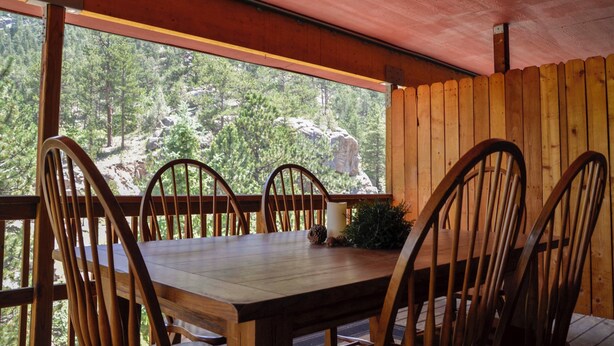 A wooden dining table with four chairs, a candle, and a small plant on a porch with a wooden railing. - Duplex Cabin at The Woolly Bugger Inn (#15) (Estes Park)