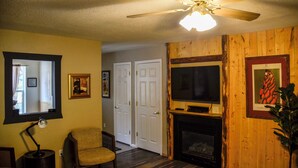 A living room with a ceiling fan, a fireplace, a television, and a chair. - Duplex Cabin at The Woolly Bugger Inn (#15) (Estes Park)
