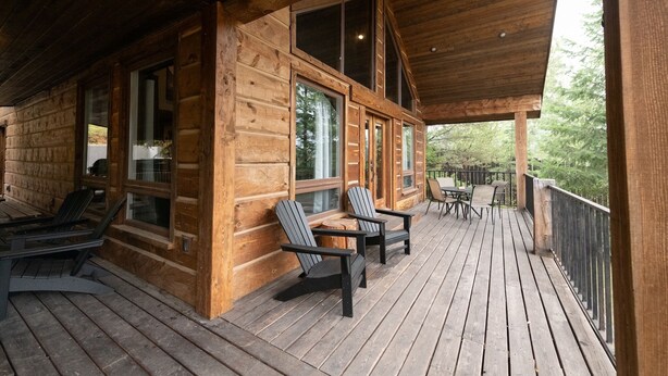 A wooden cabin with a covered porch, large windows, and outdoor seating. - Mountain Lion Den at Snowcat Cabins (Hot Tub!) (Coram)