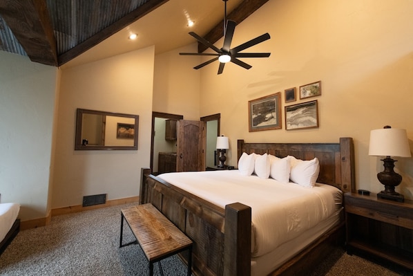 A bedroom with a wooden bed, a bench, a ceiling fan, and artwork on the walls.