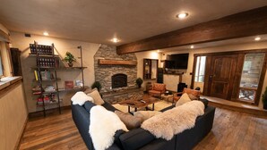 A cozy living room with a stone fireplace, a black leather sofa, and a wooden coffee table. - Mountain Lion Den at Snowcat Cabins (Hot Tub!) (Coram)