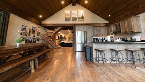A spacious kitchen with wooden flooring, a large island with bar stools, a refrigerator, and a dining area with a bench. - Mountain Lion Den at Snowcat Cabins (Hot Tub!) (Coram)