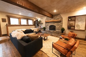A cozy living room with a stone fireplace, a sofa, a coffee table, and a leather armchair.
