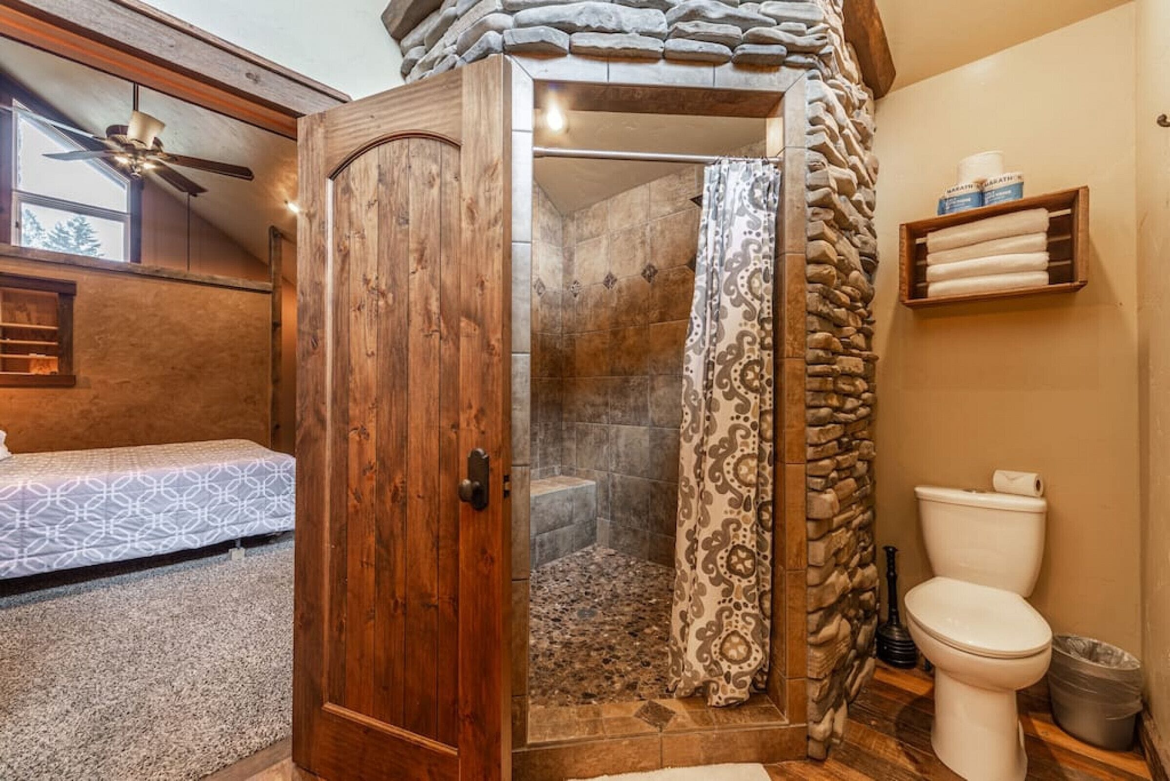 A bathroom with a shower, toilet, and a wooden door.