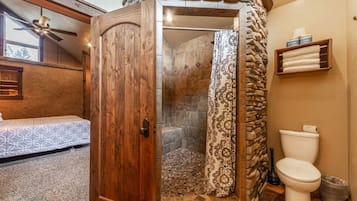A bathroom with a shower, toilet, and a wooden door.
