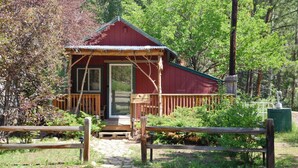 A small cabin with a wooden deck and a porch, surrounded by greenery. - Marmot Mini Cabin (Unit 7) at The Woolly Bugger Inn (Estes Park)
